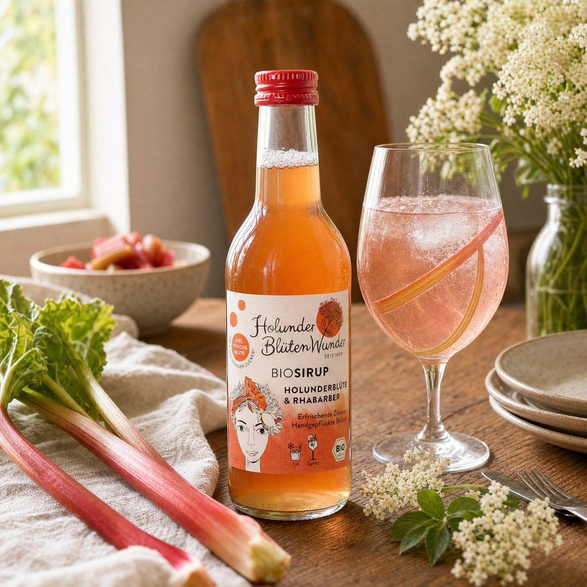 HolunderBlütenWunder Bio-Sirup Holunderblüte & Rhabarber mit einem rosa Spritz, Rhabarberstangen und Holunderblüten